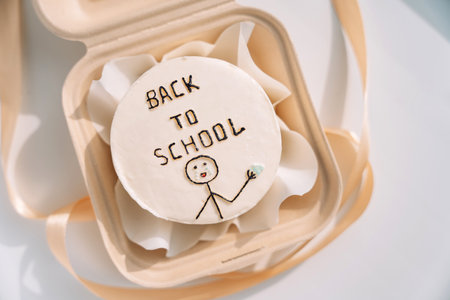 Back to school inscription on a white round cake in a gift container with a ribbonの写真素材