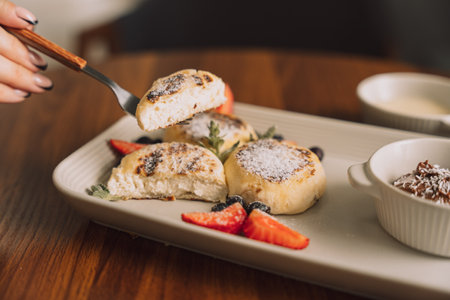Cottage cheese pancake on forks with strawberries on a rectangular plate with sauce on a wooden tableの写真素材