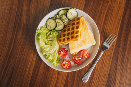 Sliced vegetables with scrambled eggs in a waffle on a white plate with a forkの写真素材