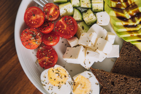 Vegetable salad with cheese and eggs and rye bread on a white plateの写真素材