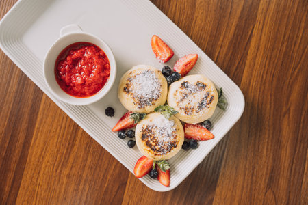 Cottage cheese pancakes with strawberries on rectangular plate with sauce on wooden tableの写真素材