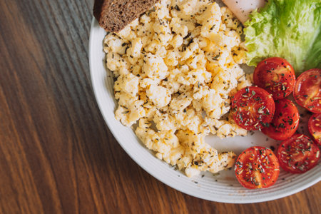 Sliced vegetables with scrambled eggs on a white plate on a wooden tableの写真素材