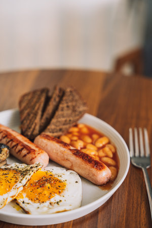 Fried eggs with sausages and rye bread on a white plate with a forkの写真素材