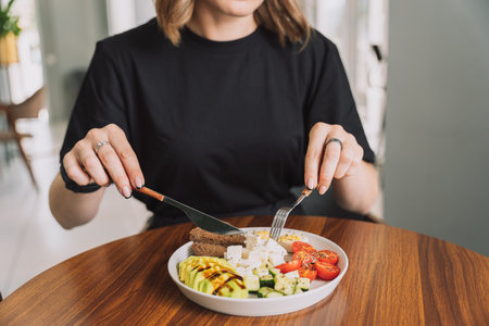 Girl has breakfast vegetable salad with cheese and eggs and rye bread on a white plateの写真素材