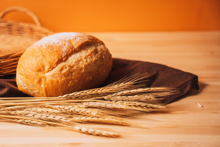 Freshly baked loaf of bread next to ears of wheat on a wooden tableの写真素材