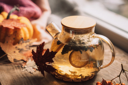 Brewed herbal tea with lemon in a glass teapot in front of a window and a pumpkinの写真素材