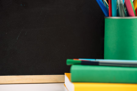 School supplies with colored books in front of the blackboardの写真素材