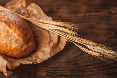 Fresh loaf of bread with ears of wheat on a wooden backgroundの写真素材