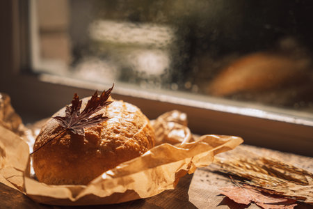 Fresh loaf of bread in paper packaging with maple leaves in front of the windowの写真素材