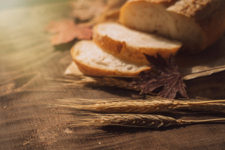 Sliced fresh loaf of bread in paper packaging with ears of wheat and maple leaves on a wooden tableの写真素材