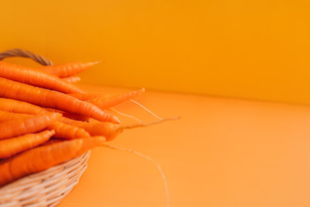 Ripe carrots in a wicker basket on an orange backgroundの写真素材