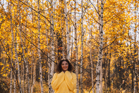 A girl in a yellow knitted sweater in front of the forestの写真素材