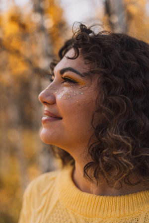 Curly girl smiling in a yellow knitted sweater in front of the forestの写真素材