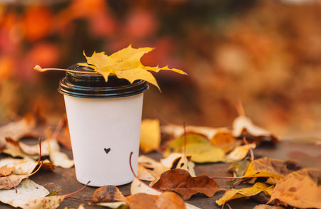 Cup of coffee with drown heart in it on the open-air lawn in front of yellow leavesの写真素材