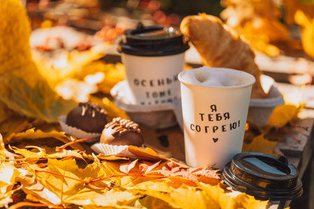 Two cups of coffee with a croissant on a wooden pallet outdoors against yellow leavesの写真素材