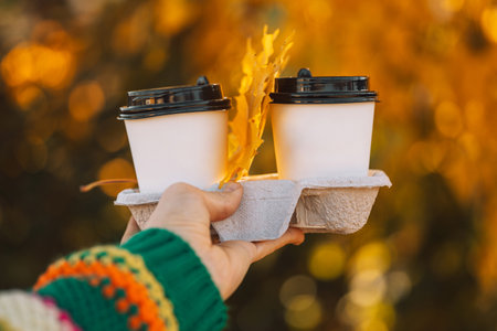 A hand in a striped sweater holding coffee in a trayの写真素材