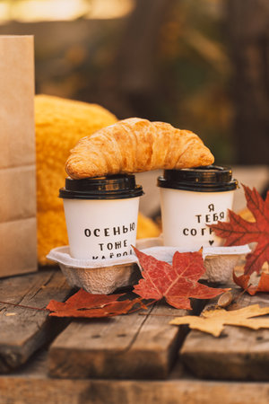 White cups with a hot drink and a croissant with red maple leaves on a palletの写真素材