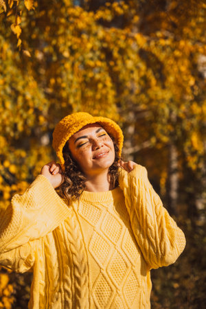 Lady in a yellow knitted sweater and hat stands under yellow birch treesの写真素材