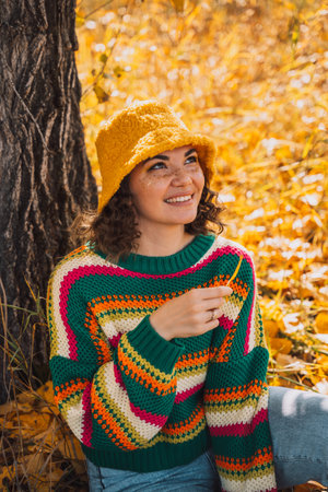 Lady in a striped knitted sweater and hat sits under a tree in the forestの写真素材
