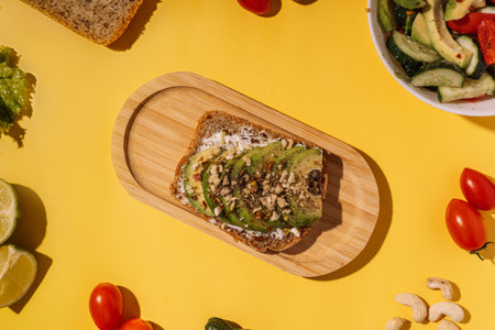 Vegetarian sandwich sprinkled with ground nuts on a wooden table among fresh vegetables on a yellow backgroundの写真素材