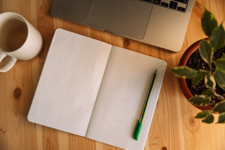 Open notepad with pen on wooden table with laptop and home flowerの写真素材