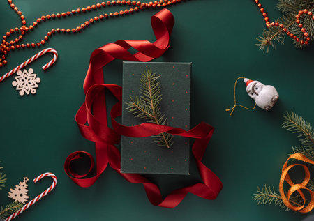 Gift in green packaging and red ribbon on a green background with a Christmas treeの写真素材