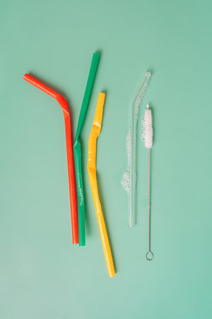 Crumpled plastic and soapy glass straws with brushes on green background