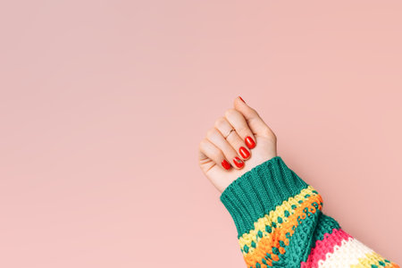 Female hands with red manicure and striped sweater against pink backgroundの写真素材