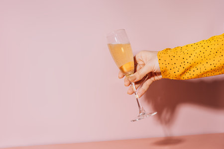 Lady hand with gold-painted nails holding a glass of champagne against a pink backgroundの写真素材