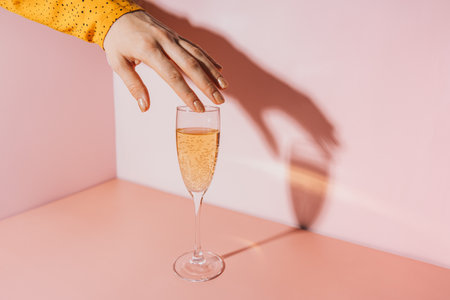 Ladys hand over a glass of champagne against a pink backgroundの写真素材