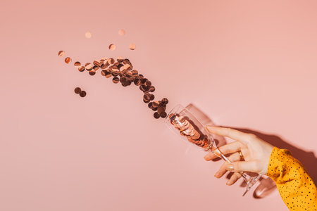 Ladys hand holding a glass from which large round sparkles fly out against a pink backgroundの写真素材
