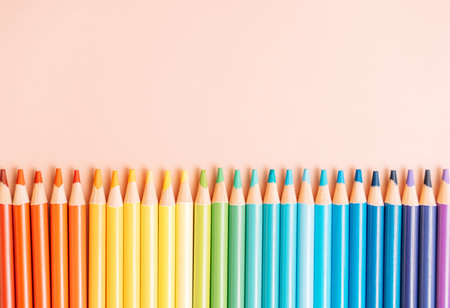 Colored rainbow pencils lie in a row on a beige backgroundの写真素材