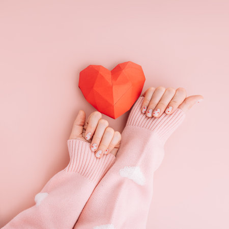 Manicure for Valentines Day with a red heart on a pink backgroundの写真素材