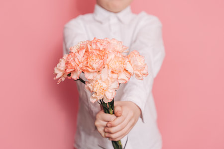 Boy in white shirt gives bouquet of carnations against pink backgroundの写真素材