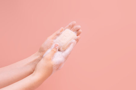 Female soapy hands holding a piece of soap against a pink background