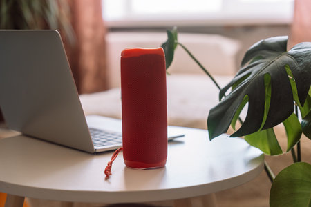 Red wireless smart speaker on white table with laptop in roomの写真素材