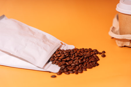 Paper cup in tray next to whole coffee beans on orange backgroundの写真素材