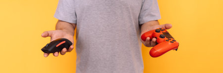 Man holding a computer mouse in one hand and gamepad in the other hand against yellow backgroundの写真素材