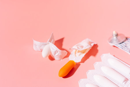 Rectal candles in packaging and unpacked and ointment in a tube on a pink background
