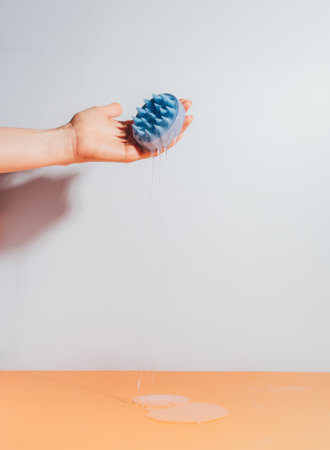 Hand holding a blue massager for the scalp and serum flows from itの写真素材
