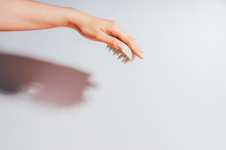 White massager for the scalp in the hand of the lady opposite the light backgroundの写真素材