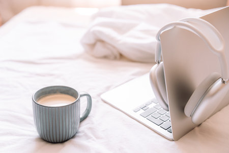 Cozy workplace with wireless headphones hanging on laptop with cup of coffeeの写真素材