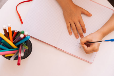 The girl writes with a pen with her left hand in a notepad on a white table