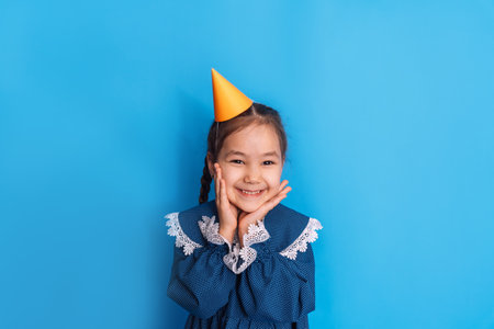 Birthday girl in a blue dress with a yellow cap on her head against a blue backgroundの写真素材