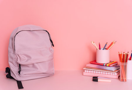 Purple backpack on a table with school supplies in front of a pink backgroundの写真素材