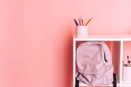 There are school supplies and a backpack on white shelves against a pink backgroundの写真素材