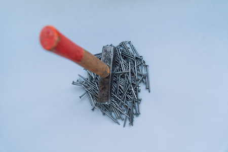 A hammer stands on a pile of nails in the middle of a gray background