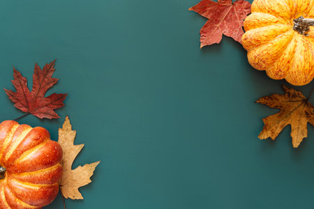 Pumpkins and dry maple leaves in the corners of a green background