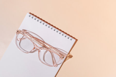 Pink eyeglasses on notebook and beige background.の写真素材