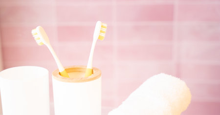 Two yellow toothbrushes in holder in bathroom on pink background